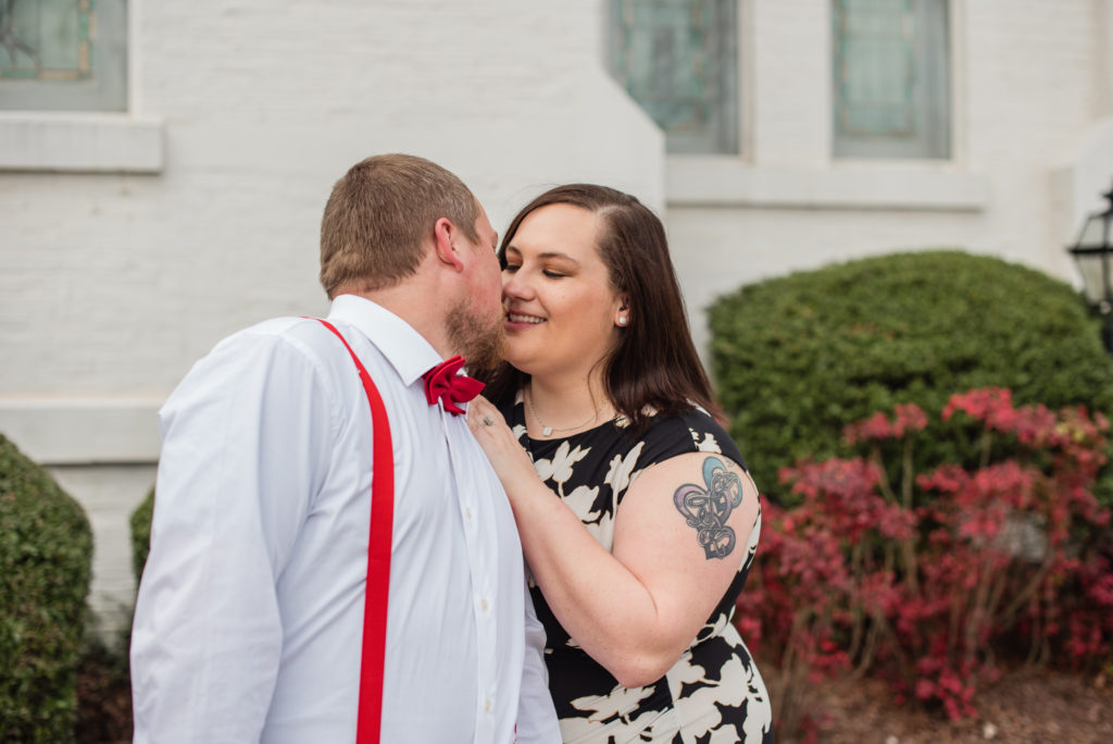 Engaged couple kissing in front of whit building and bushes in Newnan GA