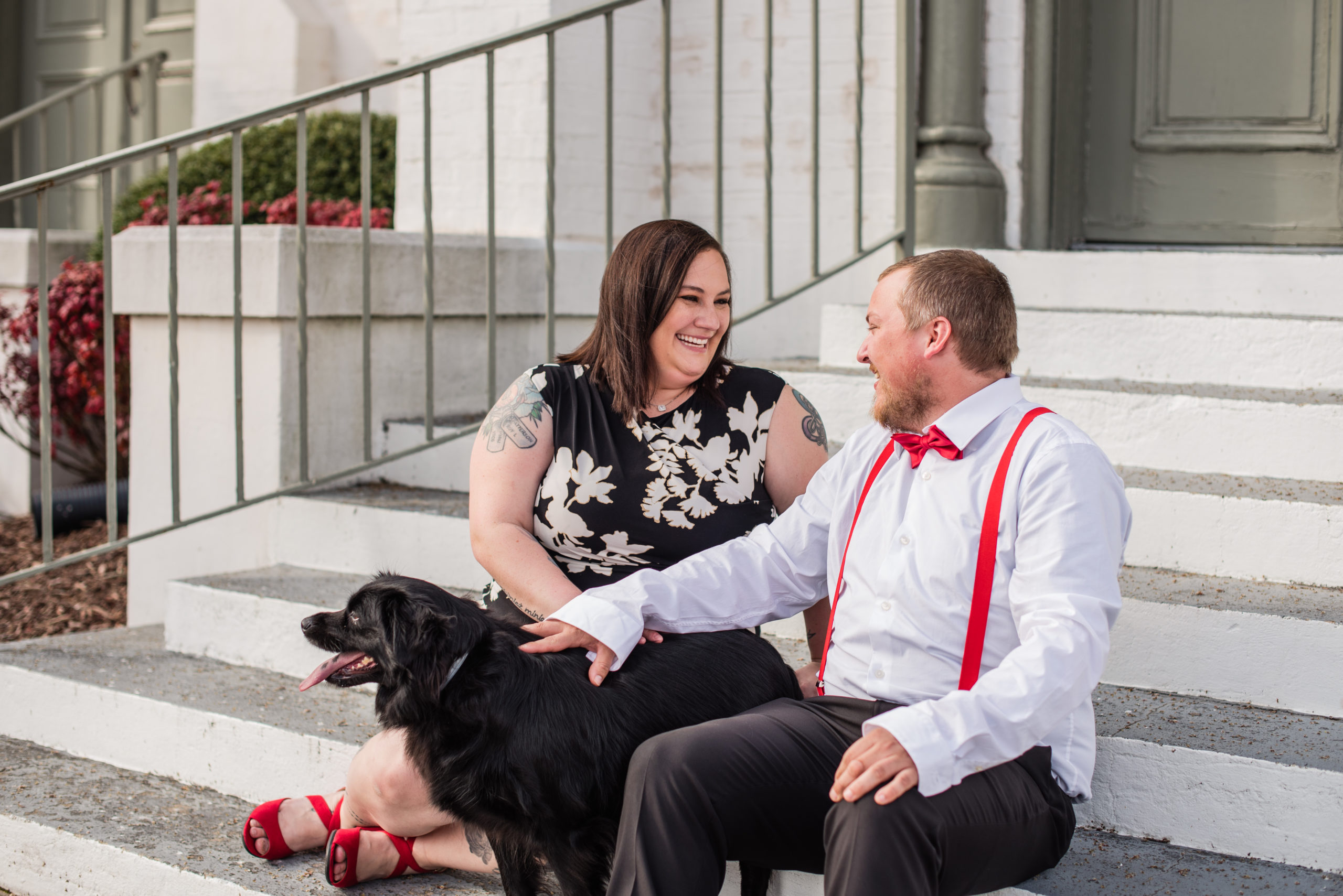 Engaged couple sitting on steps petting black dog in Newnan GA