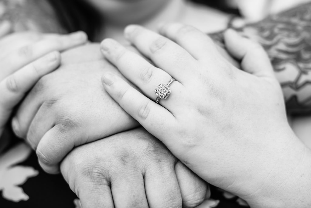 Close up black and white photo of engaged couples hands in an embrace showcasing the engagement ring