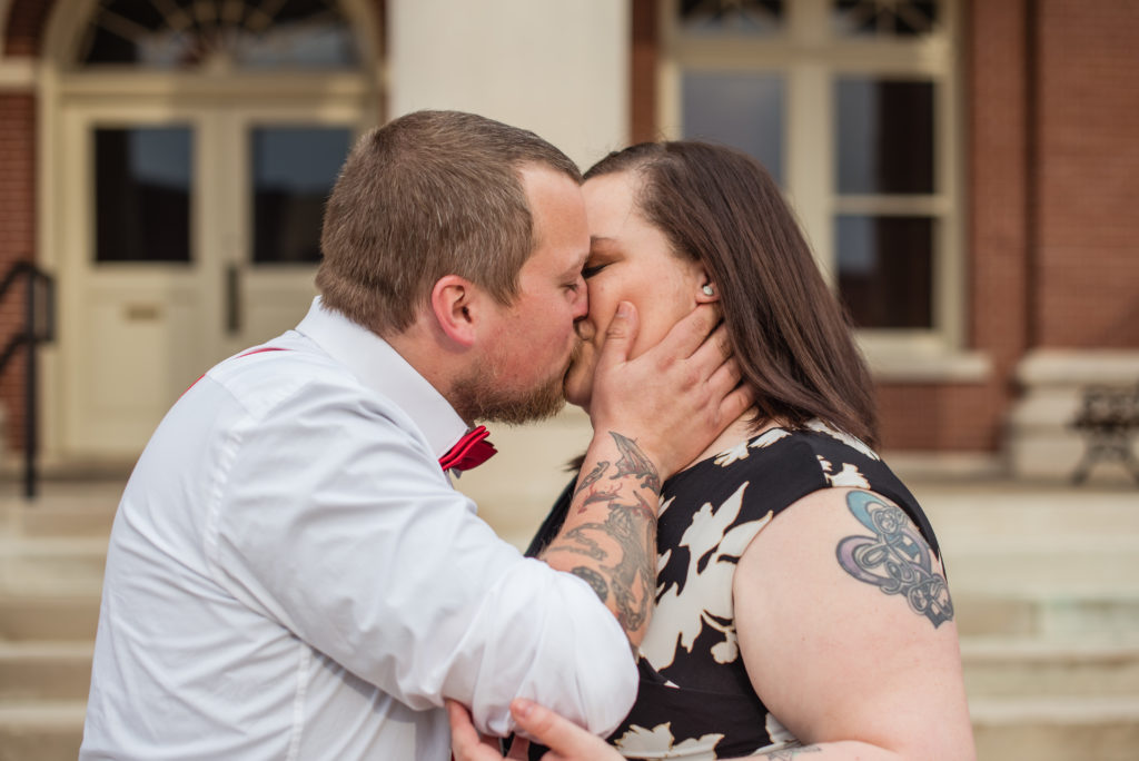 Engaged couple kissing romantically in front of courthouse in Newnan GA